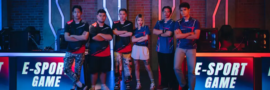 Een divers team van zes esports-spelers staat zelfverzekerd met de armen over elkaar in een gamingarena. Neonverlichting en borden met de tekst „E-Sport Game“ versterken de competitieve sfeer